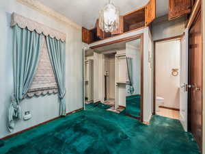 Unfurnished bedroom with dark colored carpet, connected bathroom, an inviting chandelier, and a closet