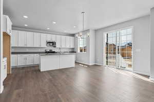 Kitchen with appliances with stainless steel finishes, decorative light fixtures, white cabinetry, hardwood / wood-style flooring, and a center island with sink