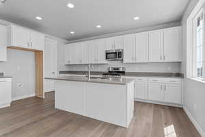 Kitchen featuring sink, appliances with stainless steel finishes, white cabinetry, an island with sink, and light wood-type flooring