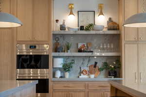 Kitchen featuring stainless steel double oven, light brown cabinetry, and backsplash