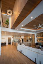 Living room with ceiling fan with notable chandelier, a high ceiling, light hardwood / wood-style floors, a raised ceiling, and wooden ceiling