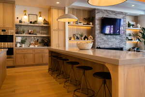 Bar with backsplash, light hardwood / wood-style flooring, stainless steel double oven, and light brown cabinets