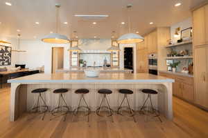 Kitchen with a breakfast bar, decorative light fixtures, light hardwood / wood-style flooring, light brown cabinets, and a large island