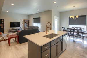 Kitchen featuring sink, dishwasher, a center island with sink, decorative light fixtures, and light wood-type flooring