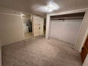 Unfurnished bedroom featuring light carpet, washer / dryer, wooden walls, and water heater