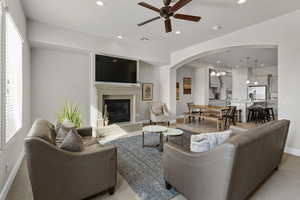 Living room with recessed lighting, ceiling fan, arched walkways, a glass covered fireplace, and light carpet
