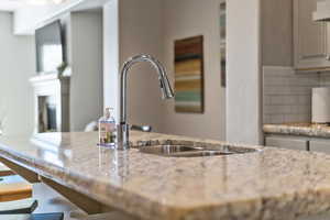 Kitchen view of a kitchen bar, light stone counters, decorative backsplash, and exhaust hood