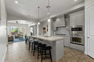 Kitchen featuring stainless steel appliances, premium range hood, a ceiling fan, backsplash, and a kitchen bar