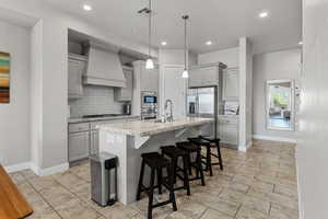 Kitchen with gray cabinetry, custom range hood, stainless steel appliances, backsplash, and recessed lighting