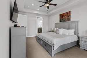 Bedroom with light carpet, recessed lighting, a raised ceiling, ensuite bathroom, and a ceiling fan