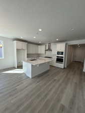 Kitchen with oven, white cabinetry, light countertops, built in microwave, and wall chimney exhaust hood