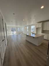 Kitchen with a center island with sink, open floor plan, white cabinets, a sink, and wood finished floors