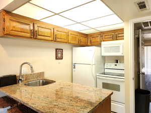 Kitchen with a kitchen bar, sink, kitchen peninsula, white appliances, and light stone countertops