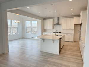 Kitchen featuring a center island with sink, wall chimney exhaust hood, and white cabinetry