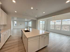 Kitchen with sink, a notable chandelier, a center island with sink, white cabinets, and light wood-type flooring