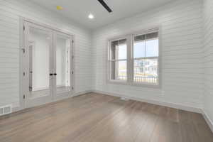 Spare room with french doors, wooden walls, and light hardwood / wood-style flooring