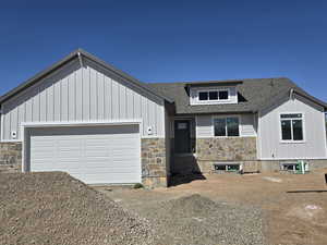 View of front of property featuring a shingled roof, board and batten siding, driveway, stone siding, and a garage