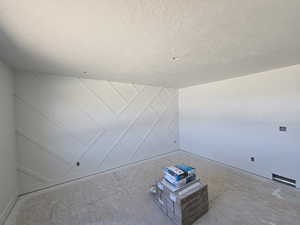 Unfurnished room featuring a textured ceiling, a decorative wall, and baseboards