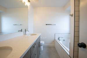 Bathroom featuring vanity, toilet, tile patterned flooring, and tiled bath