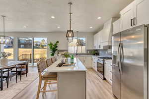 Kitchen featuring premium range hood, a breakfast bar, white cabinetry, hanging light fixtures, and appliances with stainless steel finishes