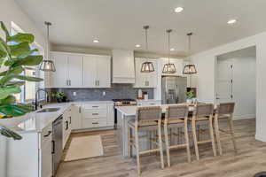 Kitchen featuring a kitchen island, decorative light fixtures, sink, stainless steel appliances, and wall chimney exhaust hood