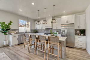 Kitchen featuring white cabinetry, custom range hood, a kitchen island, pendant lighting, and stainless steel appliances