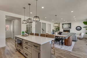 Kitchen featuring a breakfast bar, a center island, stainless steel microwave, light hardwood / wood-style floors, and decorative light fixtures