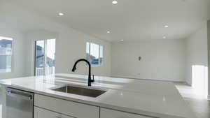 Kitchen with white cabinetry, sink, stainless steel dishwasher, and light stone counters