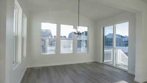 Unfurnished dining area featuring an inviting chandelier, hardwood / wood-style flooring, and vaulted ceiling