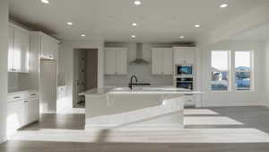 Kitchen featuring a kitchen island with sink, wall chimney range hood, sink, and white cabinets