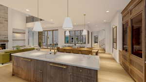 Kitchen featuring sink, hanging light fixtures, a large fireplace, a large island with sink, and light wood-type flooring