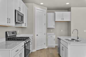 Kitchen with sink, light hardwood / wood-style flooring, stainless steel appliances, and white cabinets