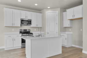 Kitchen with sink, appliances with stainless steel finishes, a kitchen island with sink, white cabinetry, and light hardwood / wood-style floors