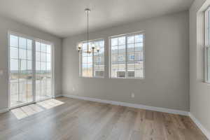 Unfurnished dining area with light hardwood / wood-style flooring, a wealth of natural light, and an inviting chandelier