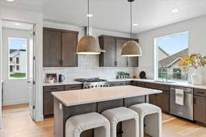 Kitchen featuring decorative light fixtures, sink, a center island, stainless steel dishwasher, and dark brown cabinetry