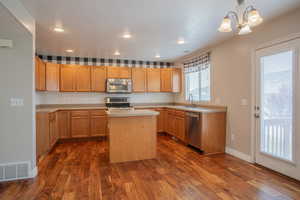 Kitchen featuring appliances with stainless steel finishes, sink, hanging light fixtures, a center island, and dark wood-type flooring