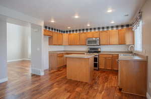 Kitchen featuring dark wood-type flooring, appliances with stainless steel finishes, a center island, and sink