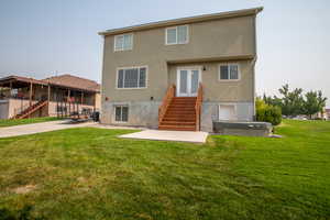 Back of house with a hot tub, a patio area, and a lawn