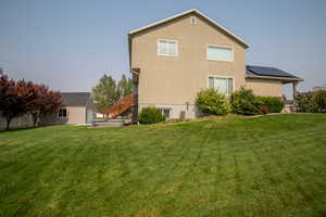 Rear view of house featuring an outdoor structure, central air condition unit, a lawn, and solar panels