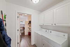 Clothes washing area with cabinets, washing machine and clothes dryer, and hardwood / wood-style flooring