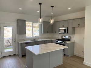 Kitchen featuring gray cabinets, appliances with stainless steel finishes, sink, a center island, and light stone counters. Finishes are subject to change