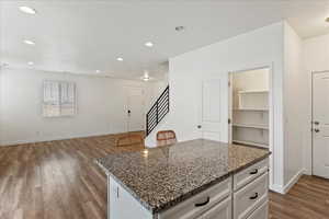 Kitchen with light hardwood / wood-style flooring, stone counters, a kitchen island, white cabinets, and a textured ceiling