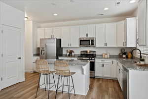 Kitchen featuring appliances with stainless steel finishes, a center island, white cabinets, and light stone counters