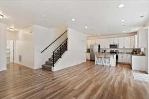 Kitchen featuring light hardwood / wood-style flooring, a kitchen island, stainless steel appliances, white cabinets, and a kitchen bar