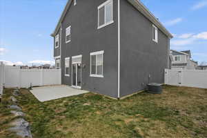 Rear view of house with central AC unit, a patio area, and a lawn