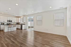 Kitchen with a kitchen bar, a center island, appliances with stainless steel finishes, light hardwood / wood-style floors, and white cabinets