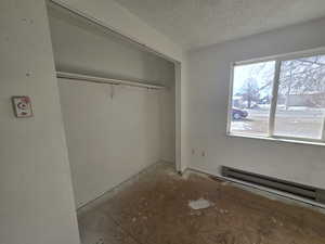 Unfurnished bedroom with a baseboard radiator, a closet, and a textured ceiling