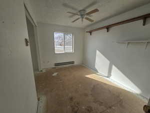 Empty room with ceiling fan, a baseboard radiator, and a textured ceiling