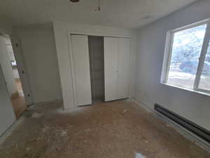 Unfurnished bedroom with a baseboard radiator, a closet, and a textured ceiling