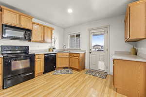 Kitchen with light hardwood / wood-style floors, sink, and black appliances